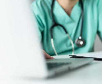 Nurse at a desk taking notes with pen, paper, and laptop